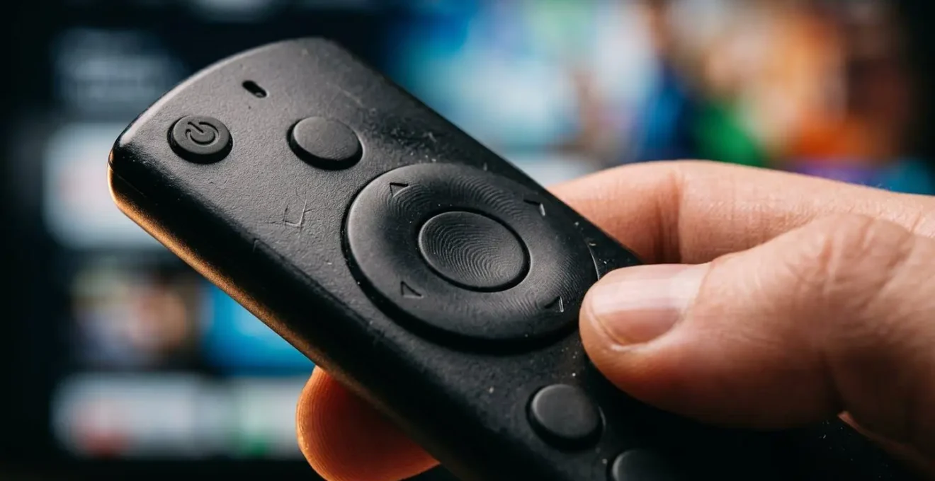 Vista macro de control remoto de TV con códigos QR difusos en pantalla de fondo